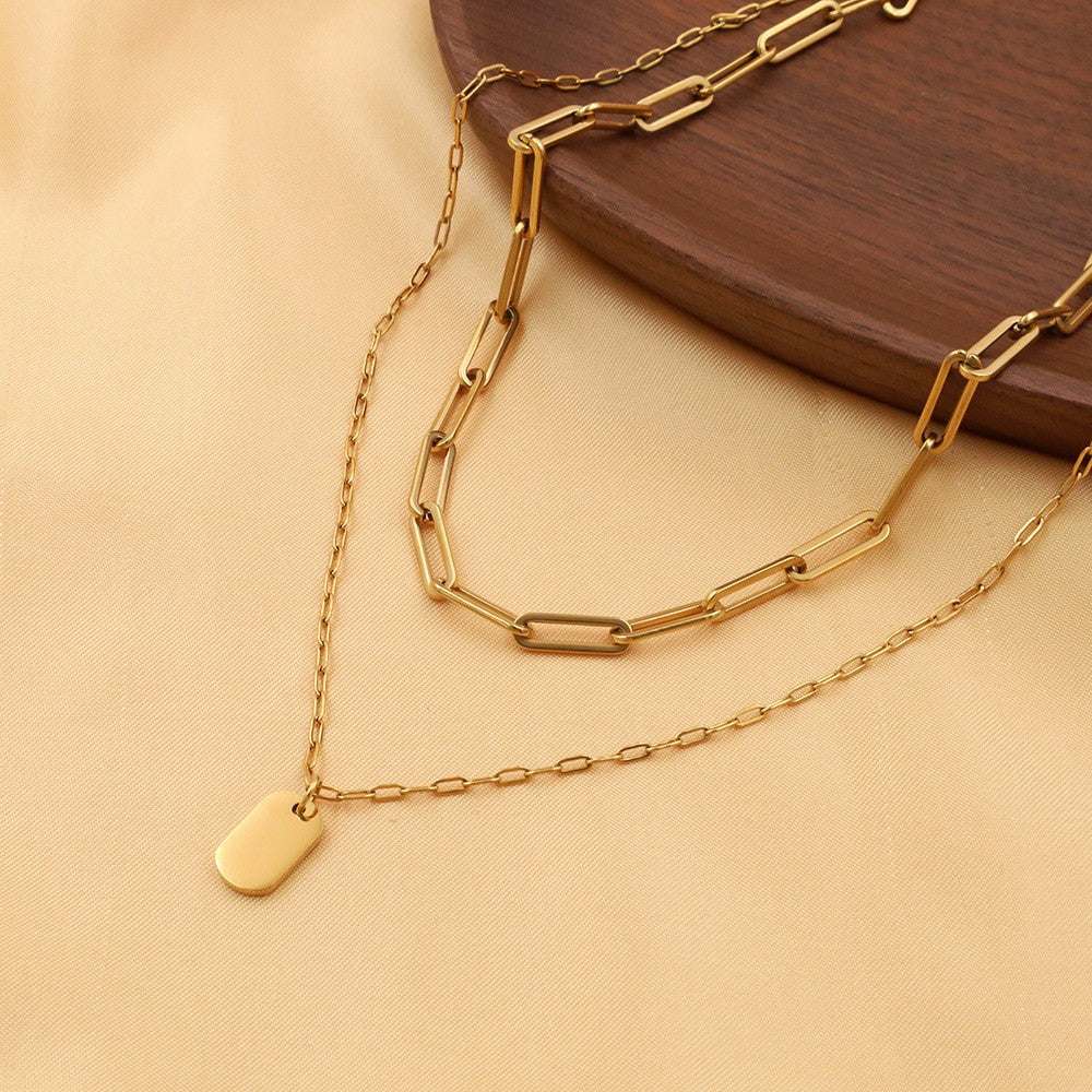 18K gold layered paperclip link and tag charm necklace flat lay on fabric