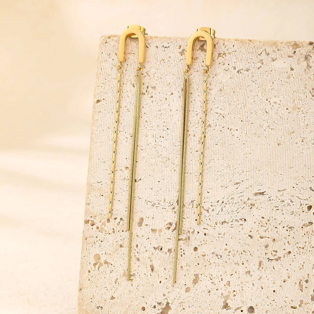 The Meche gold arch tassel earrings displayed on stone block