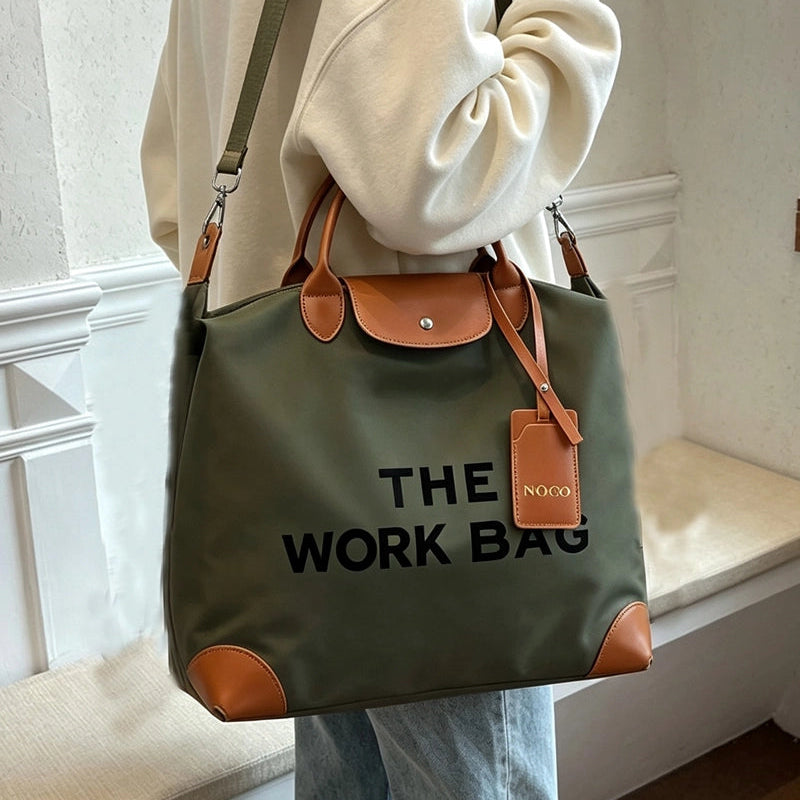 Olive Caryall The Work Bag with brown handles and trim, black lettering, and an adjustable shoulder strap worn by a model